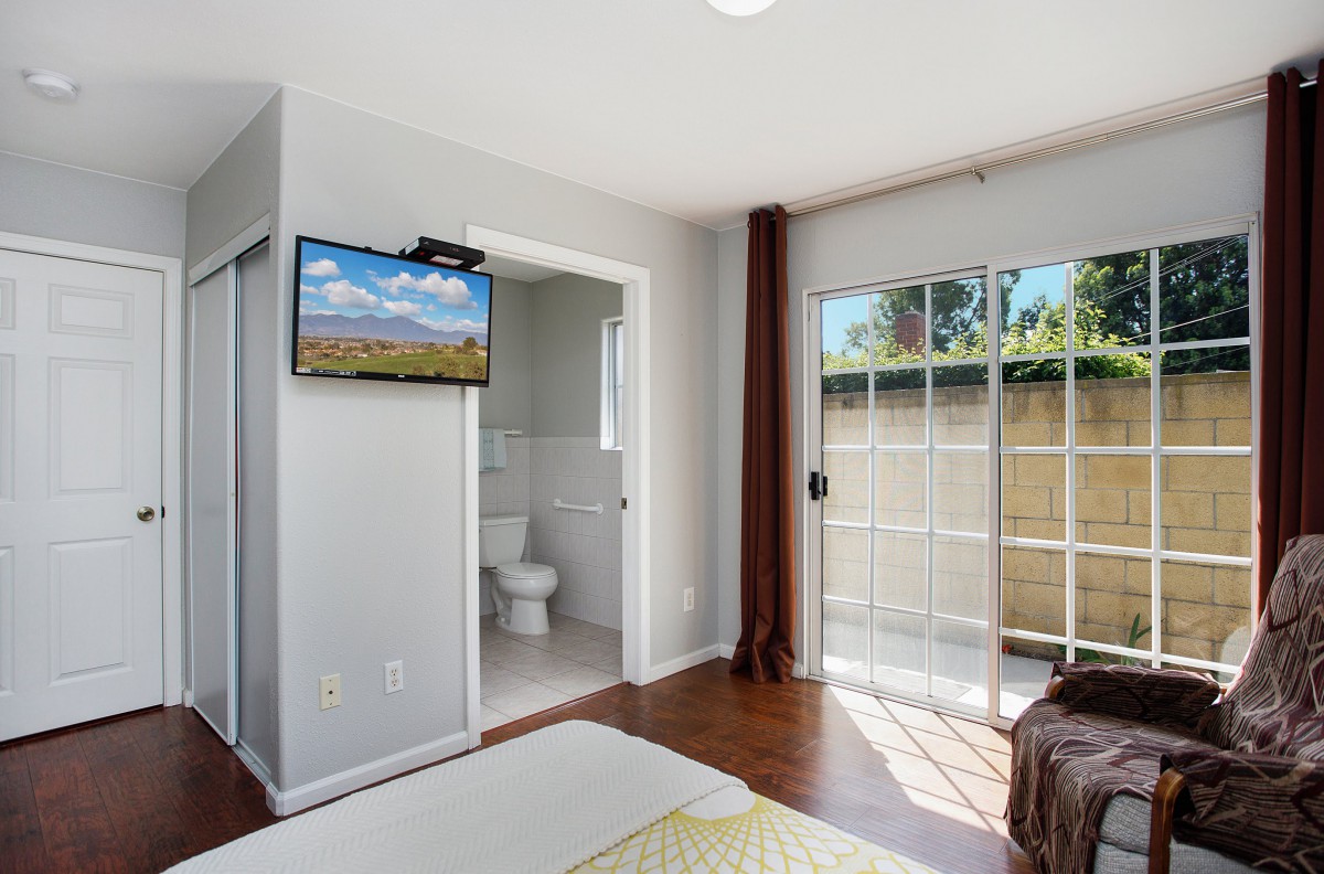 A modern, minimalist bedroom featuring a mounted TV and sliding glass doors leading to an outdoor space.
