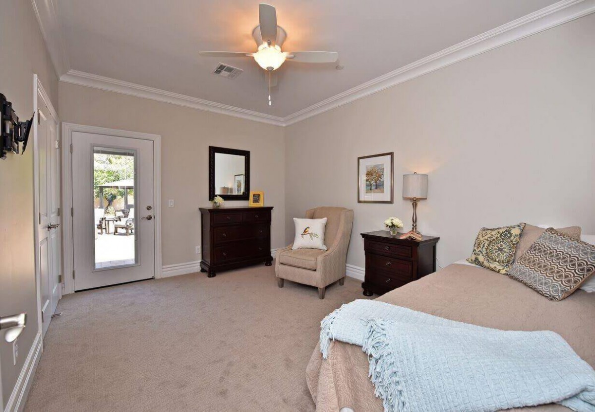 A modern bedroom with neutral decor, featuring a comfortable chair and a bedside lamp.