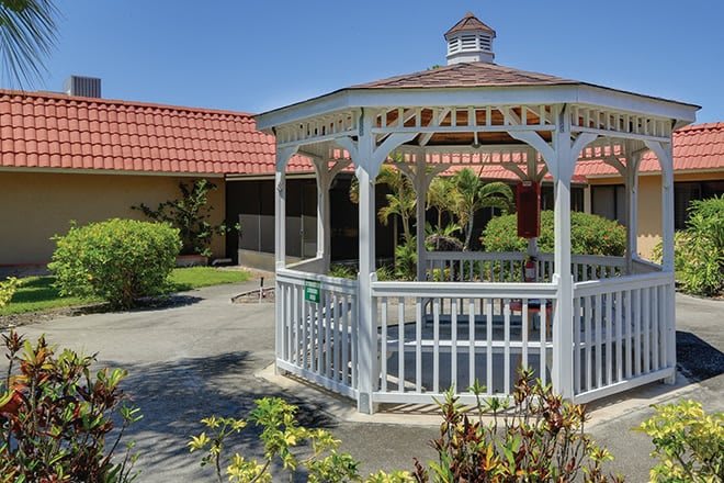 A white gazebo in a landscaped garden setting on a sunny day.
