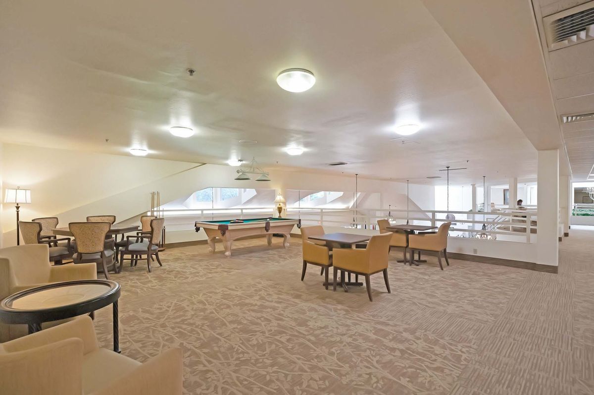 A spacious dining area with tables, chairs, and carpeted flooring under ceiling lights.