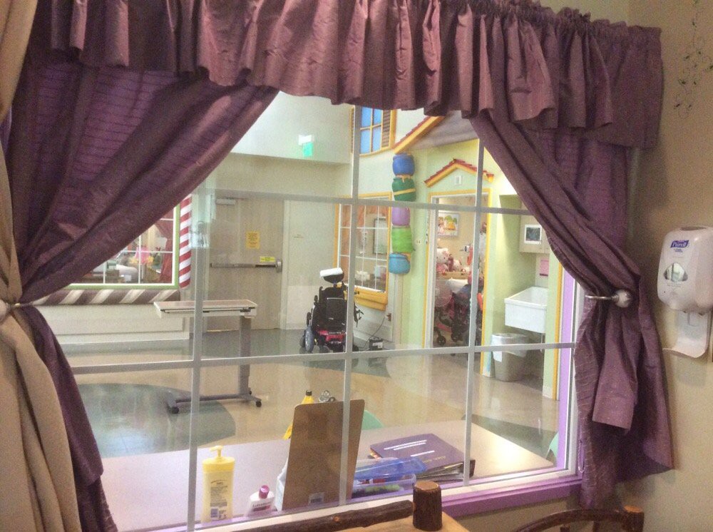 View from inside a room with purple curtains looking out to a hospital hallway where a person in a wheelchair is visible.