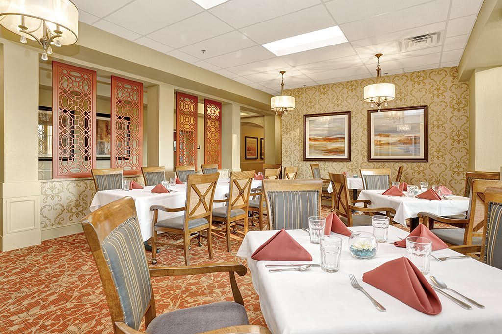 Elegant dining room with neatly arranged tables and chairs, featuring warm decor and chandeliers.