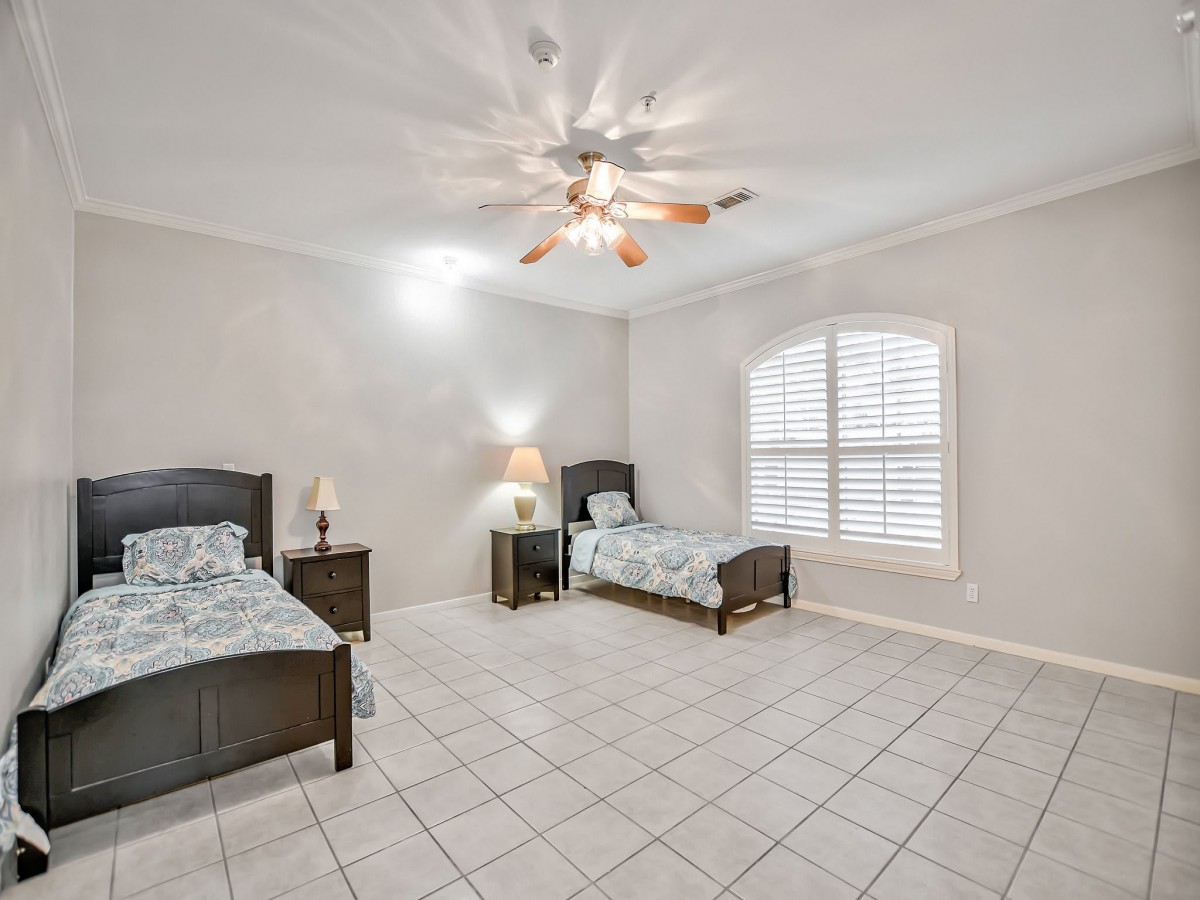 A spacious bedroom with two twin beds, tiled flooring, and a ceiling fan.
