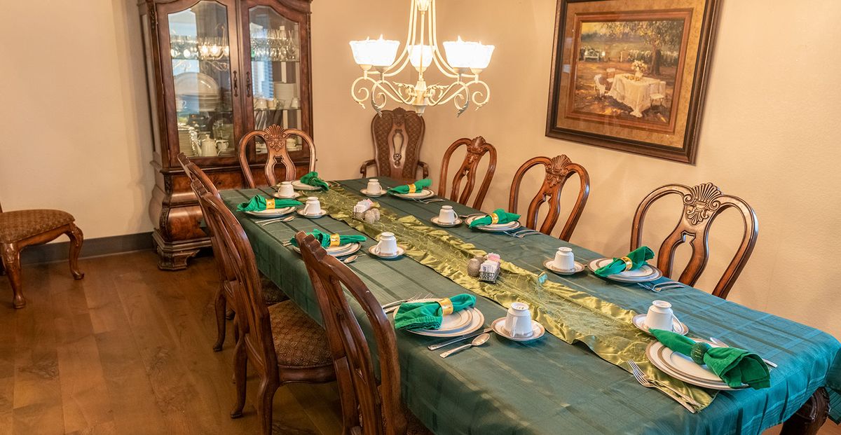A formal dining room with a long table set for a meal, featuring elegant wooden chairs, a chandelier, and neatly arranged tableware.