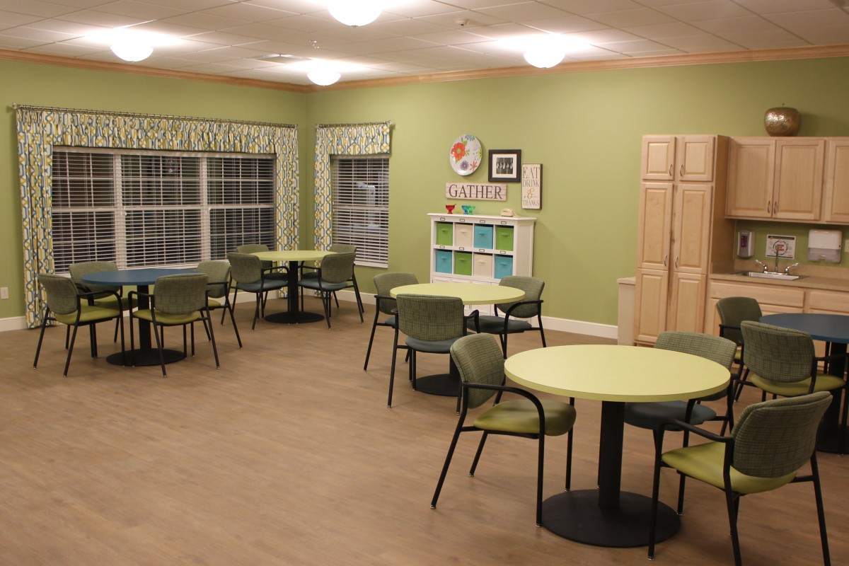 A well-lit dining area with green walls, featuring multiple tables and chairs.