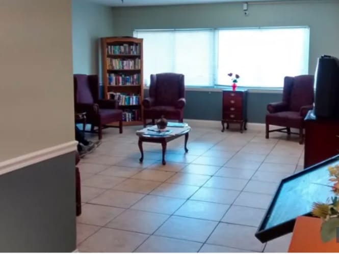 A tidy waiting room with cushioned chairs, a small table, and a bookshelf against the wall.