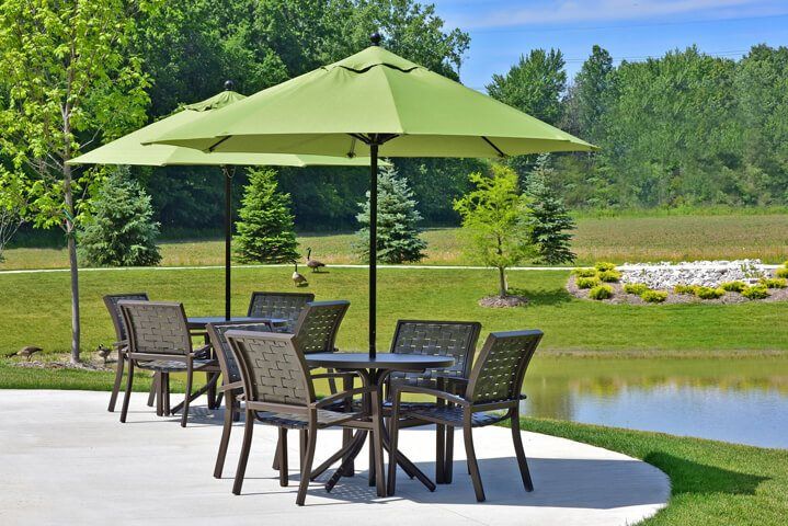 An outdoor seating area with a green umbrella overlooking a serene garden and lake.