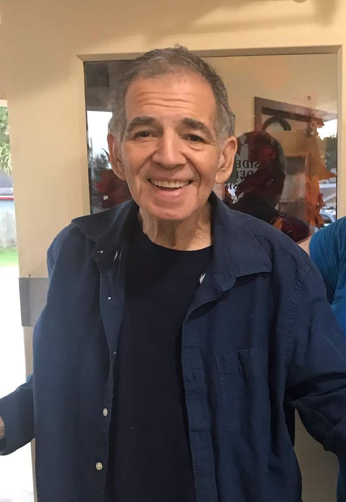 A man smiling indoors, wearing a jacket.