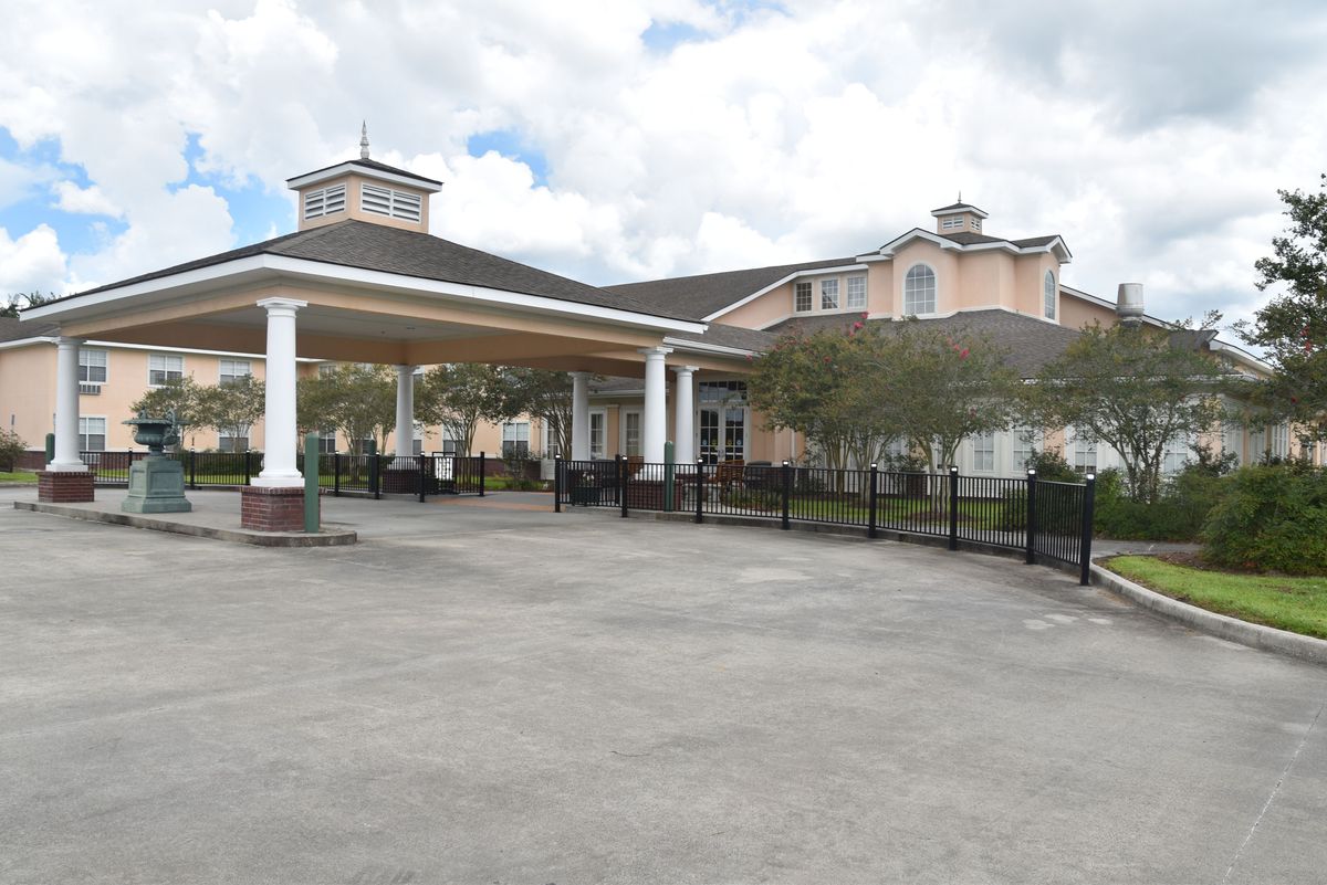 A large, two-story building with a covered driveway and landscaped surroundings under a cloudy sky.