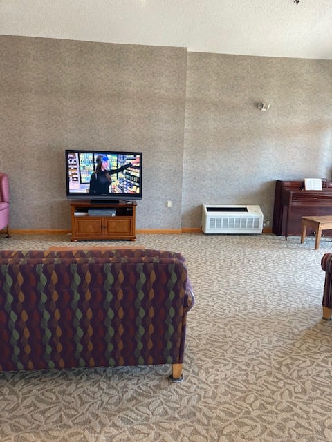 A living room with a television, piano, couch, and armchair.