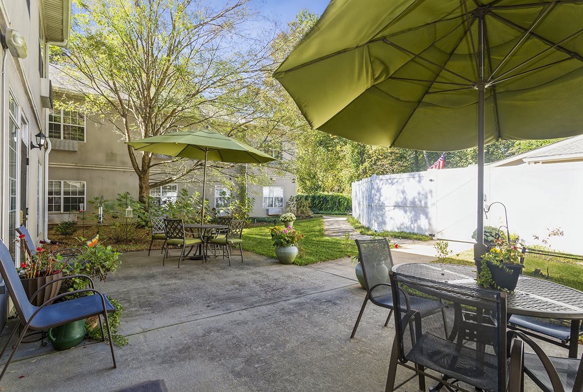 A sunny backyard patio with tables, chairs, and umbrellas surrounded by a garden.