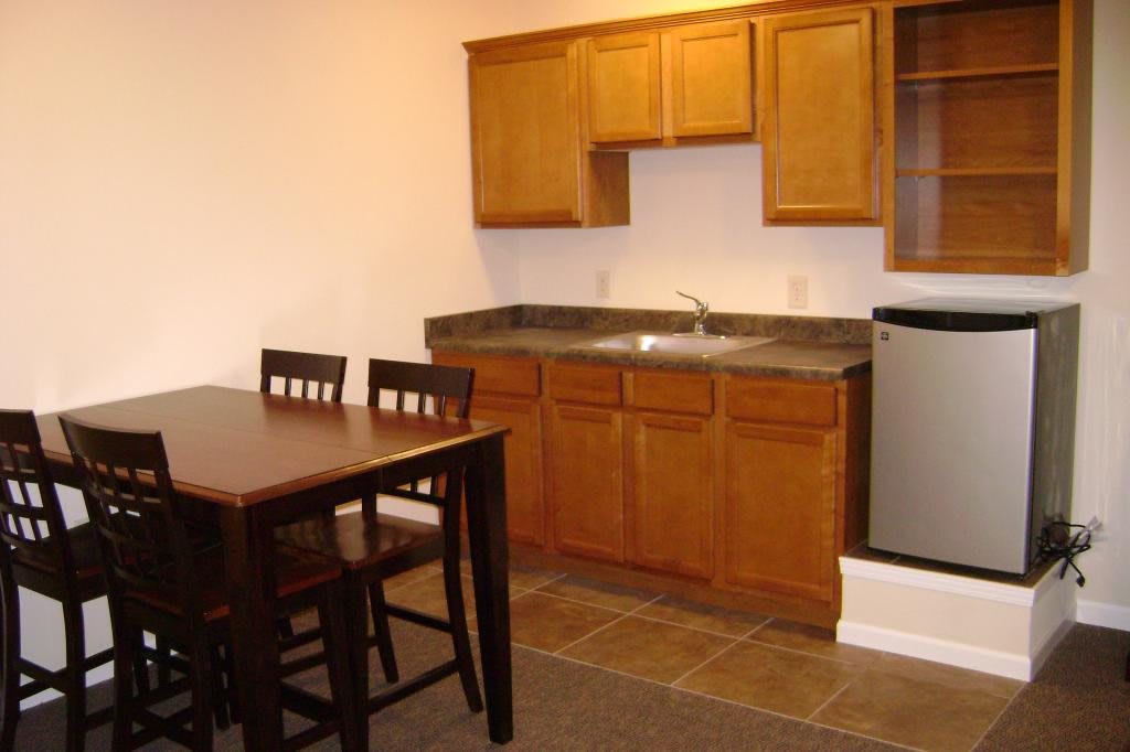 A small kitchen area with wooden cabinets, a dining table, and chairs.