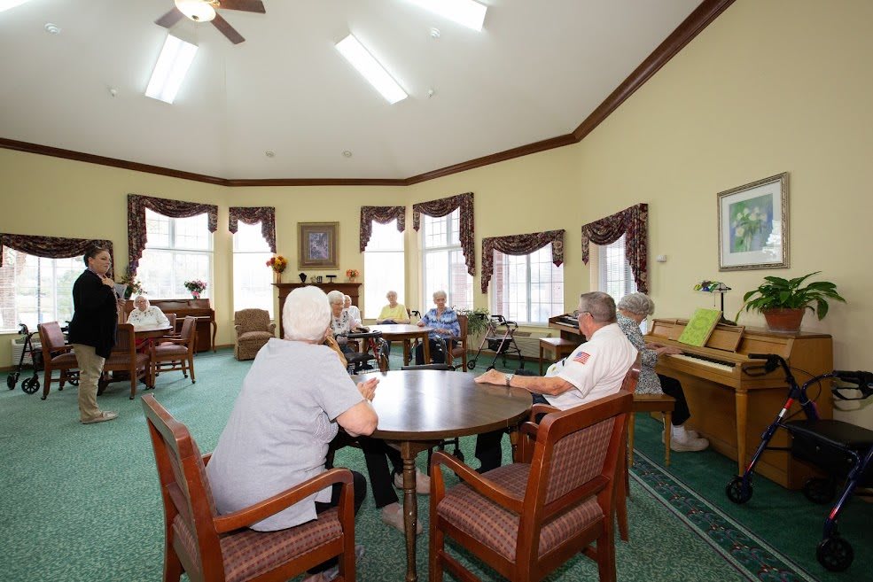 A group of seniors socializing in a community room with chairs and tables.