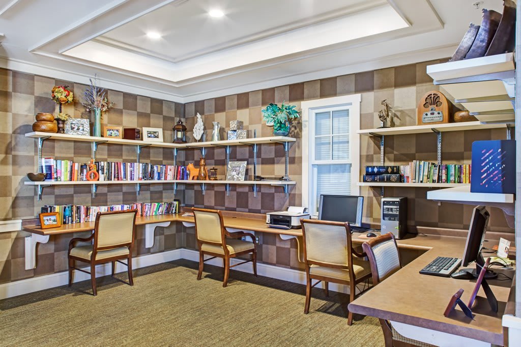 A modern office space featuring bookshelves, multiple desks and chairs, and a computer setup.