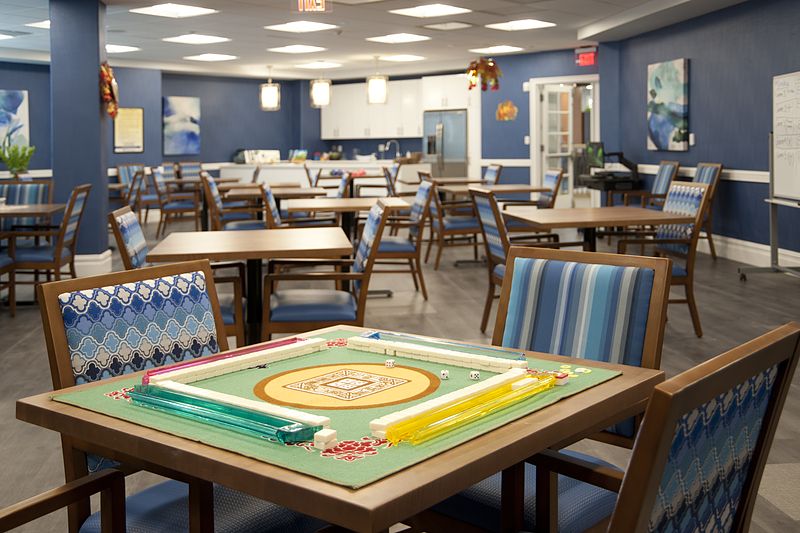 A spacious recreation room featuring a mahjong table and several seating areas.