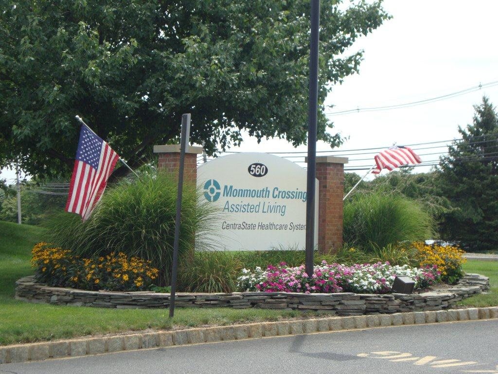 Entrance sign with American flags and landscaped flowers.
