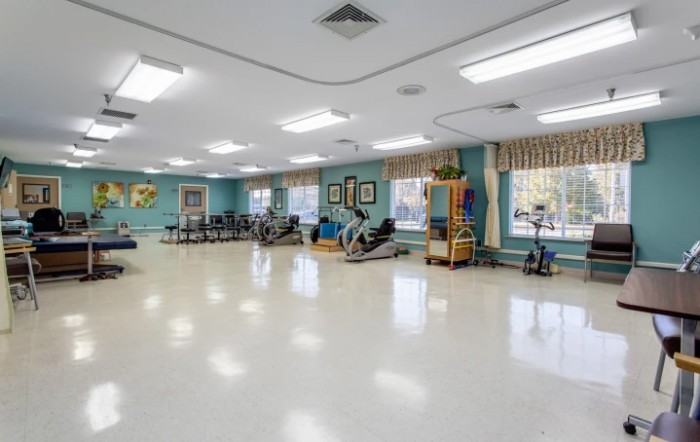 A spacious exercise room with various gym equipment and bright lighting.