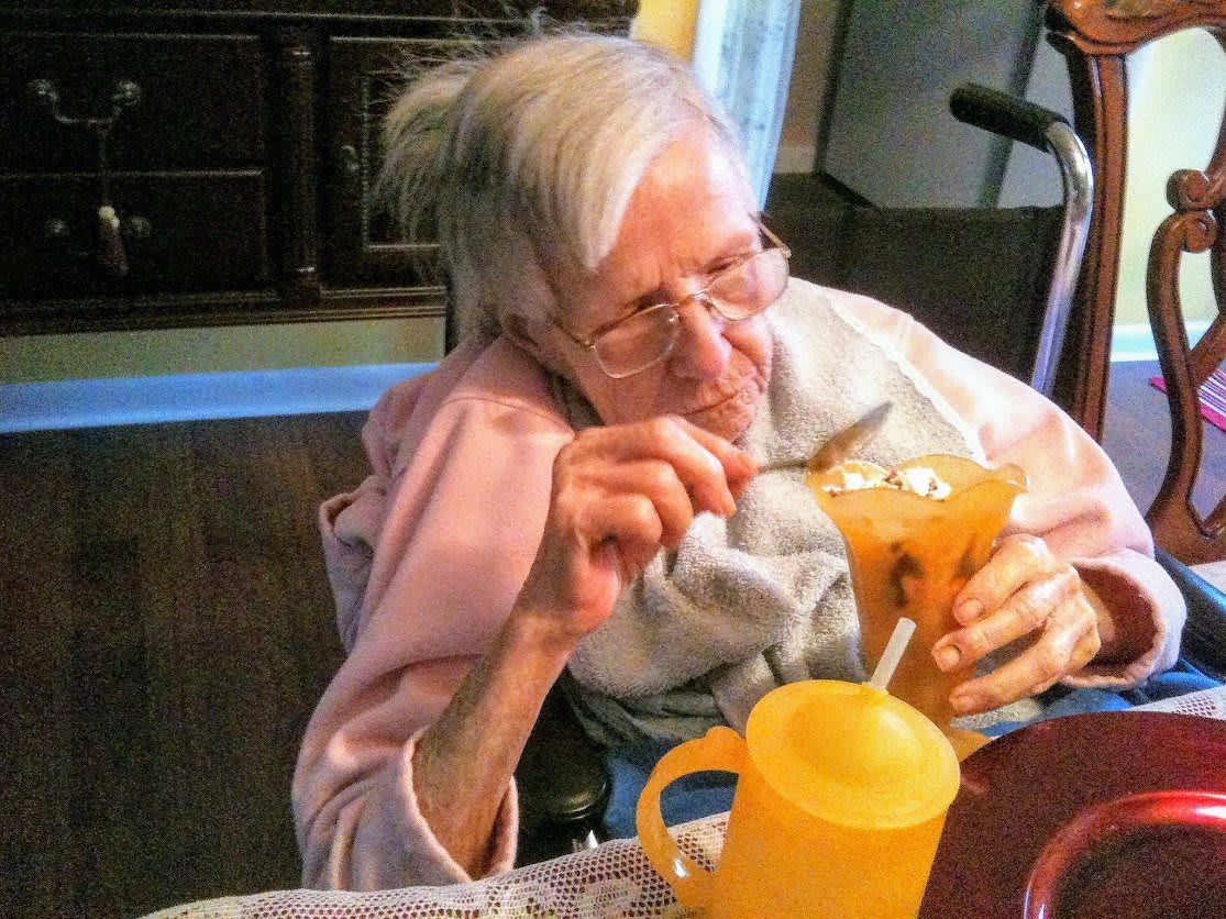 Elderly woman enjoying a dessert with a spoon.