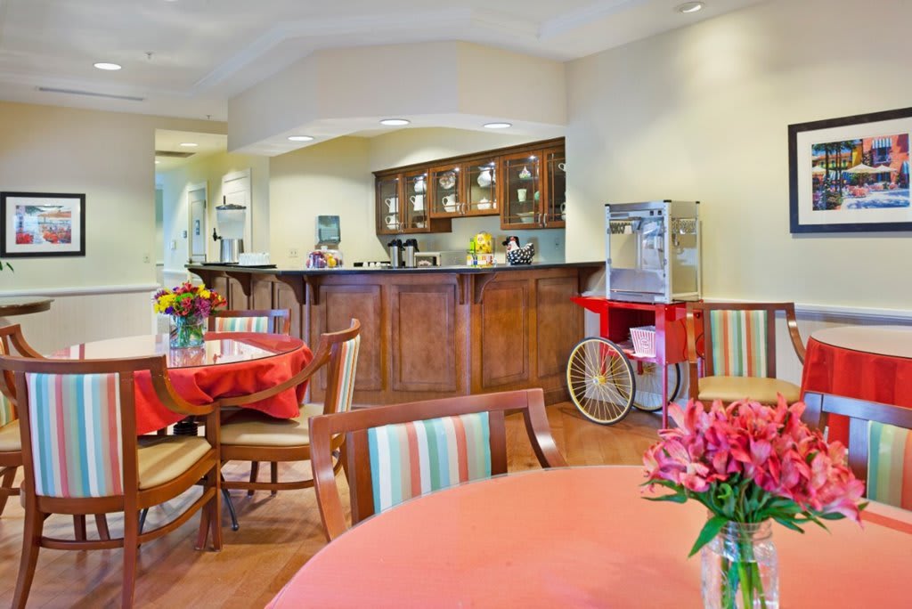 A cozy dining area featuring tables adorned with flowers and a popcorn machine near a wooden kitchen counter.