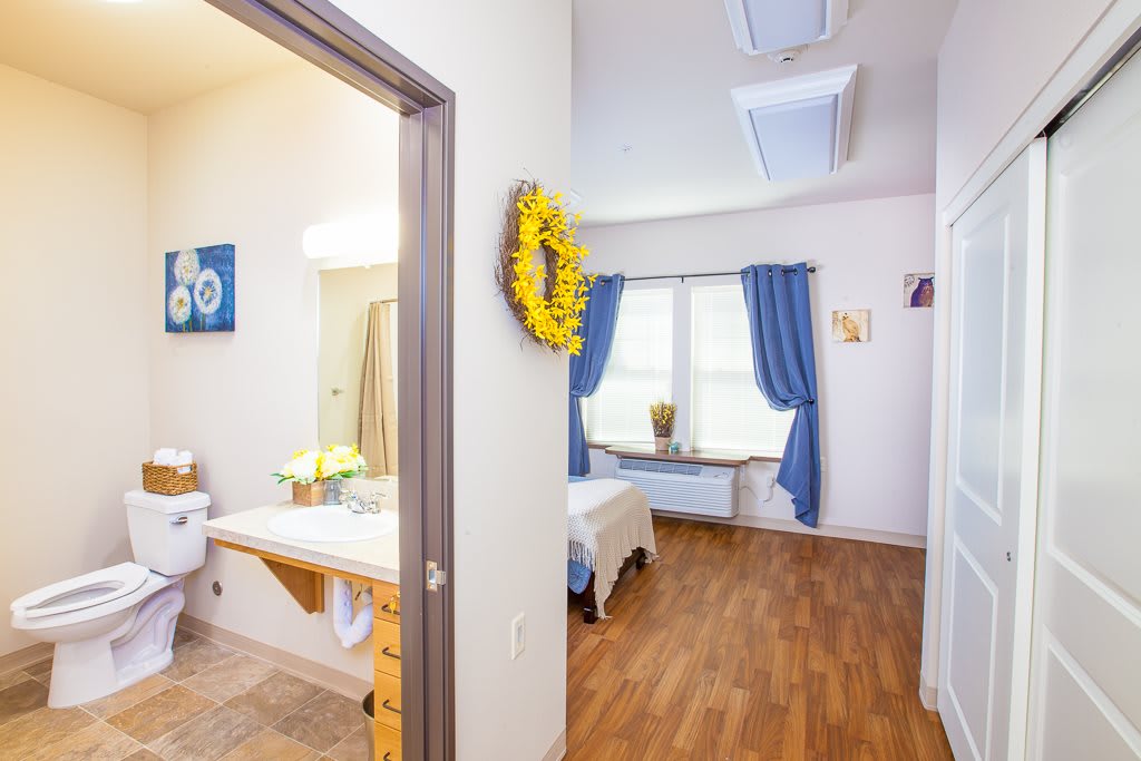 A cozy bedroom with a wooden floor, blue curtains, and a connected bathroom.