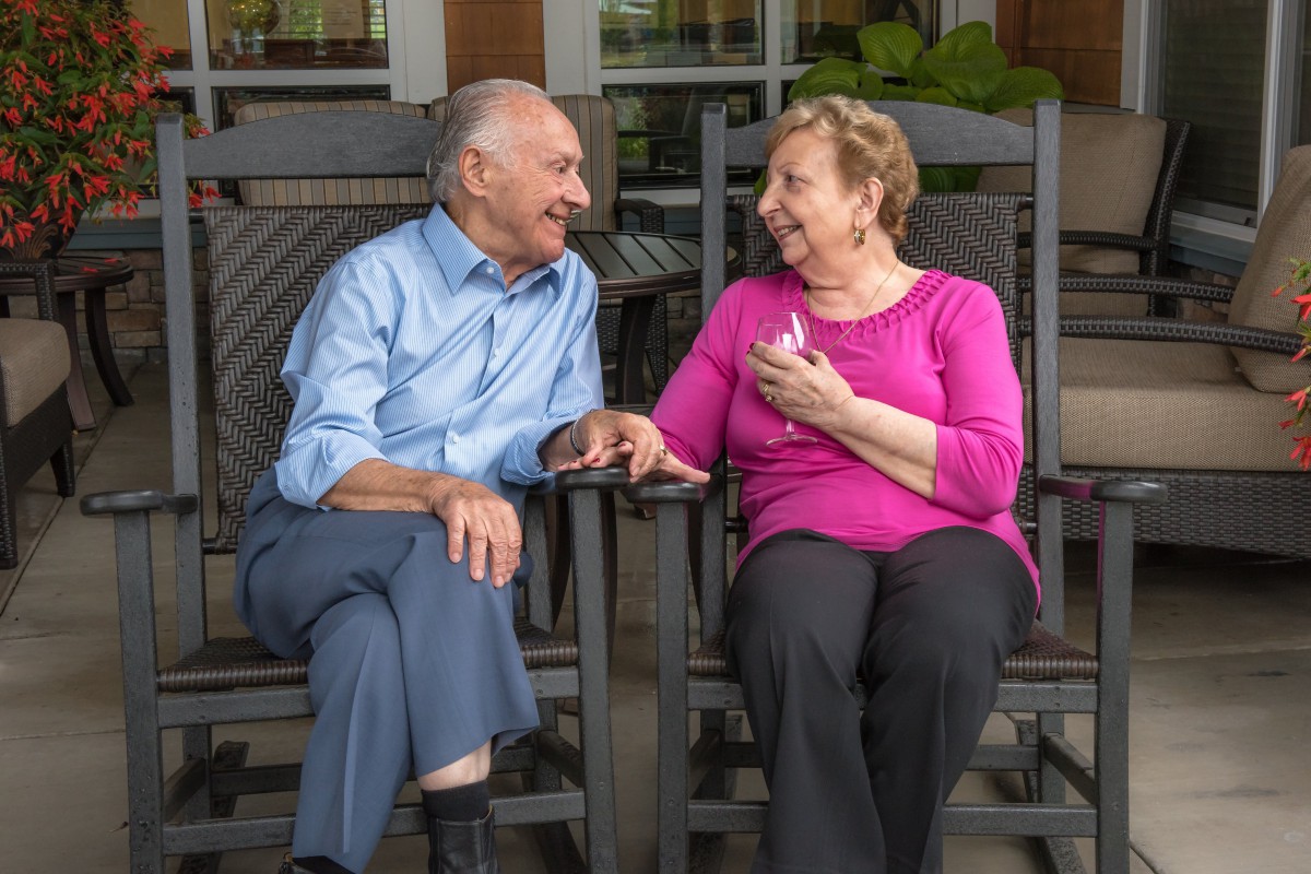 An elderly couple enjoying a conversation while sitting on rocking chairs.