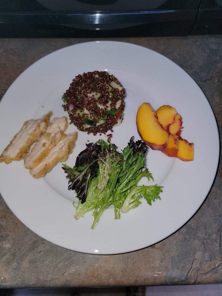 A plated dish with sliced chicken, a quinoa salad, mixed greens, and peach slices.