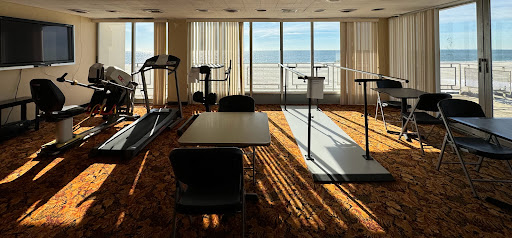 A well-lit fitness area with treadmills and tables, offering a scenic view of the ocean.