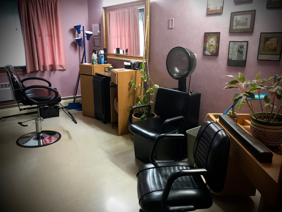 A cozy hair salon with chairs, a mirror, and a hair dryer in the corner.