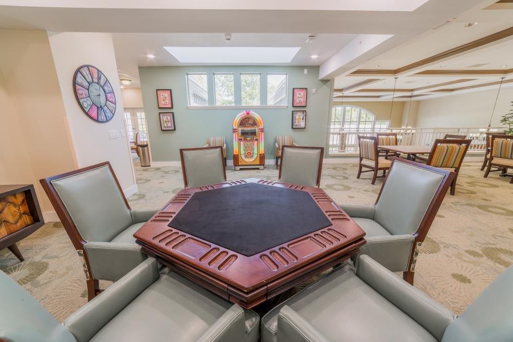 A cozy game room featuring a poker table surrounded by chairs and a vintage jukebox in the background.