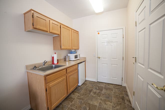 A small kitchen area with wooden cabinets, a sink, and a microwave on the counter.