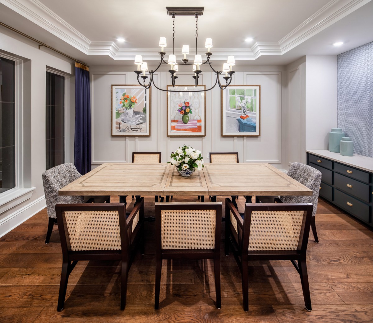 A beautifully designed dining room with a large rectangular table, surrounded by elegant chairs and adorned with a classic chandelier and artwork on the walls.