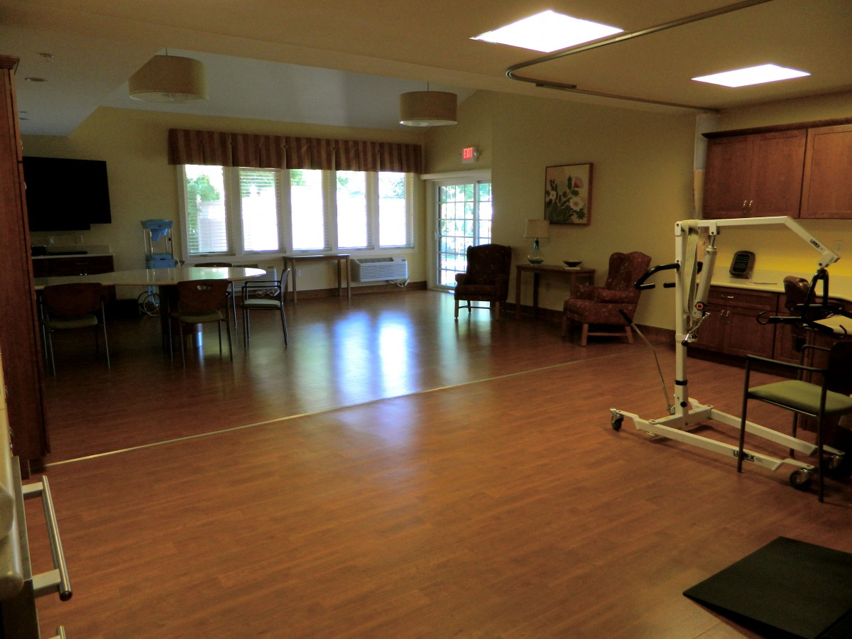 A spacious living area with hardwood floors, featuring chairs and tables under bright lighting.