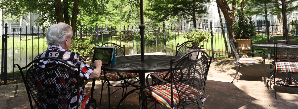A cozy outdoor patio setting with a table and cushioned chairs under an umbrella, surrounded by greenery.