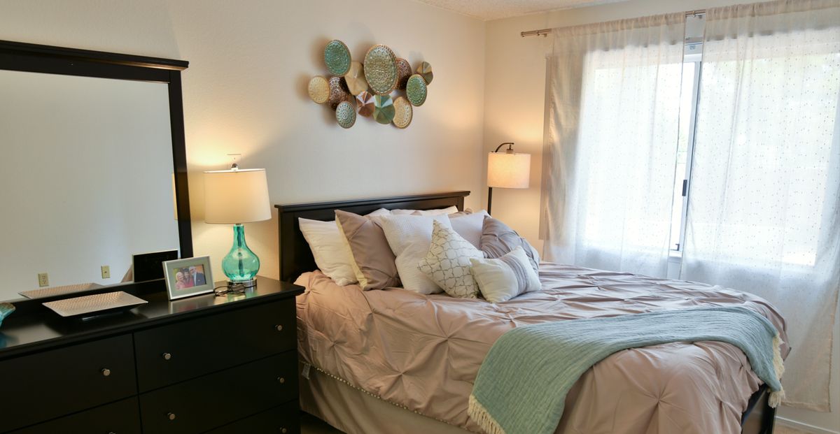 A cozy bedroom with soft lighting, featuring a neatly made bed adorned with multiple pillows and decorative wall art.