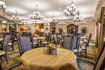 An elegantly designed dining room with multiple tables, chairs, and ornate chandeliers.