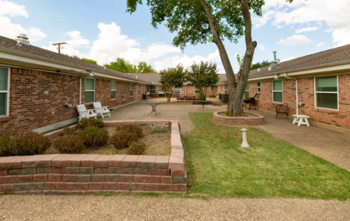 A serene courtyard in an apartment complex with brick buildings, featuring outdoor seating and landscaping.
