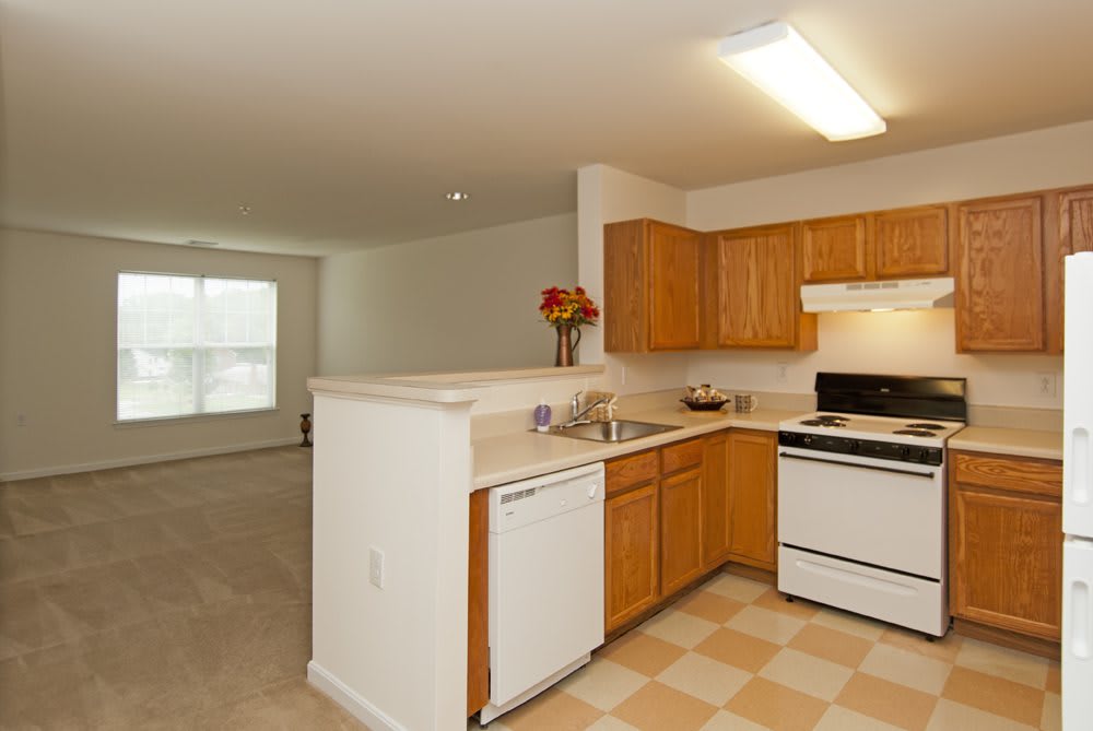 A modern apartment kitchen with wooden cabinets and an open living space.