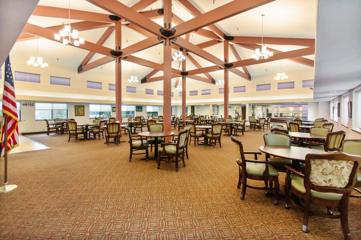 An empty, spacious dining hall with numerous tables and chairs arranged neatly under a high ceiling.
