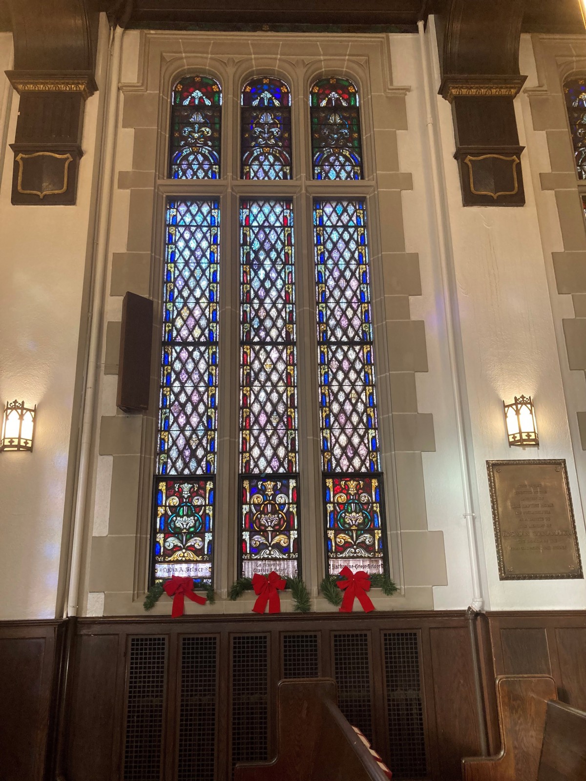 A beautifully designed church interior featuring tall stained glass windows adorned with festive decorations.