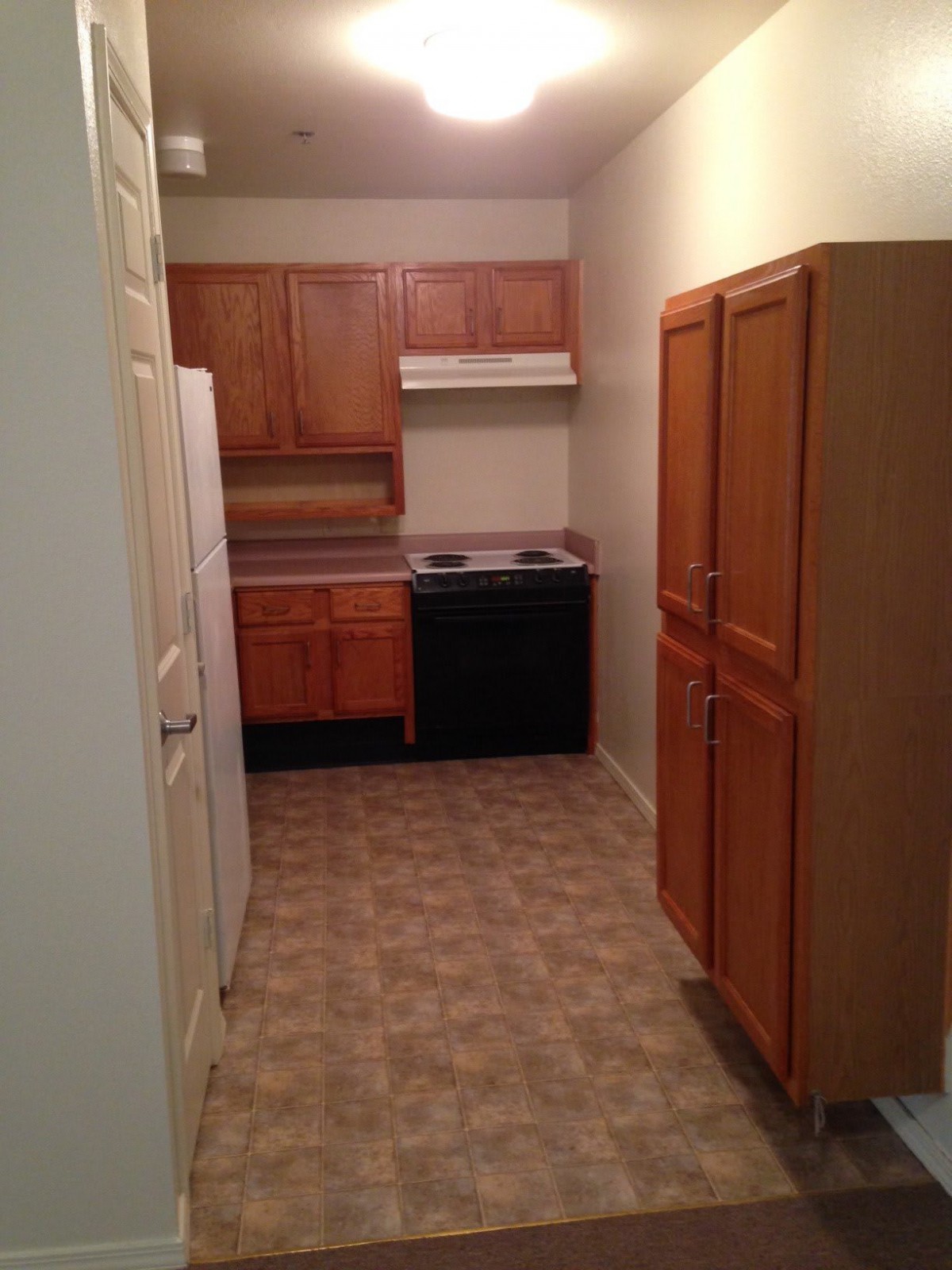 A compact apartment kitchen with wooden cabinets, a stove, and refrigerator.