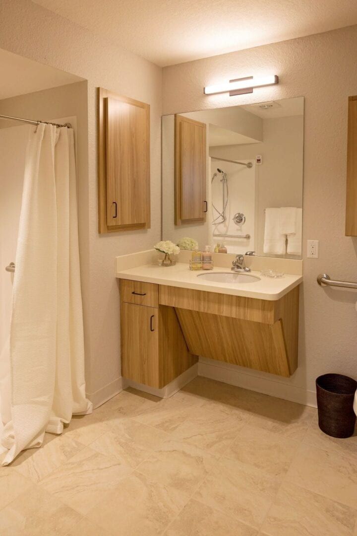 A modern bathroom with wooden cabinets, a large mirror, and a shower area.