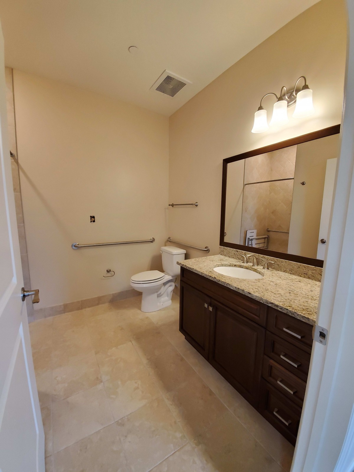 A spacious bathroom featuring a large mirror, vanity with sink, toilet, and overhead lighting.