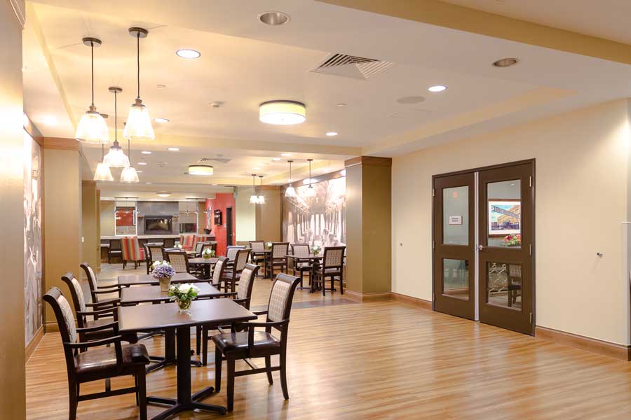 A modern and spacious dining area with wooden flooring, elegant lighting, and neatly arranged tables and chairs.