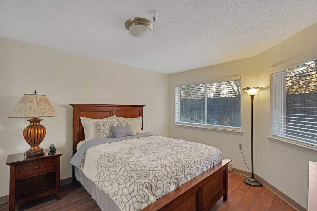 A cozy bedroom with a wooden bed frame, patterned bedding, and a floor lamp by the window.