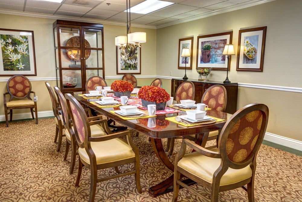 A well-decorated dining or conference room with a large wooden table set for a meal and adorned with flowers, surrounded by chairs and illuminated by a chandelier.