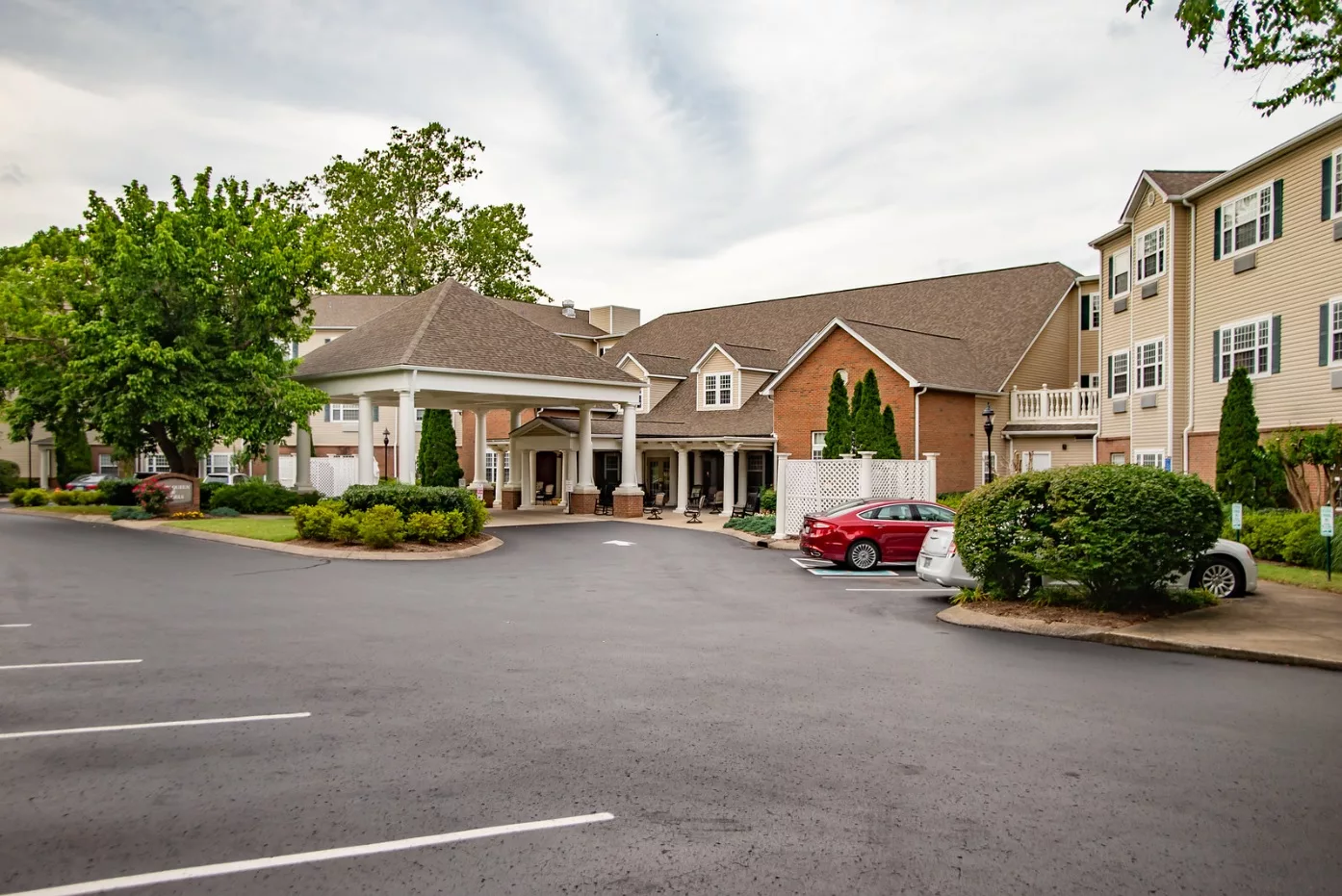 A hotel entrance with a parking lot and surrounding greenery.