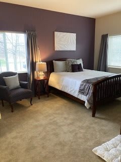 A cozy and well-decorated bedroom featuring a comfortable bed, armchair, and soft lighting.