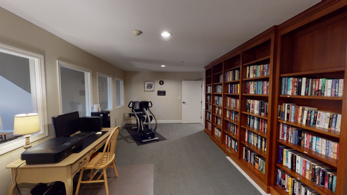 A cozy room featuring a large bookshelf, a treadmill, and a computer desk.