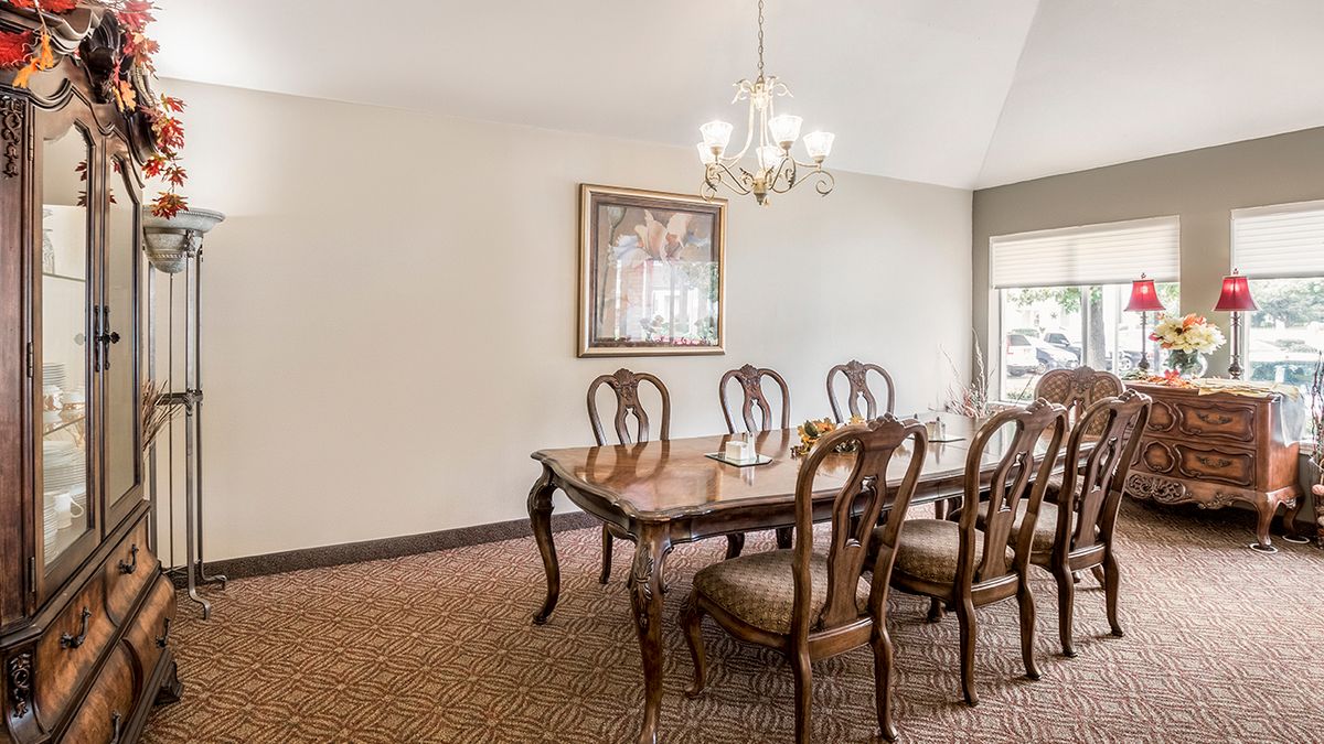 A traditional dining room with a wooden table and chairs, a chandelier above, and artwork on the wall.