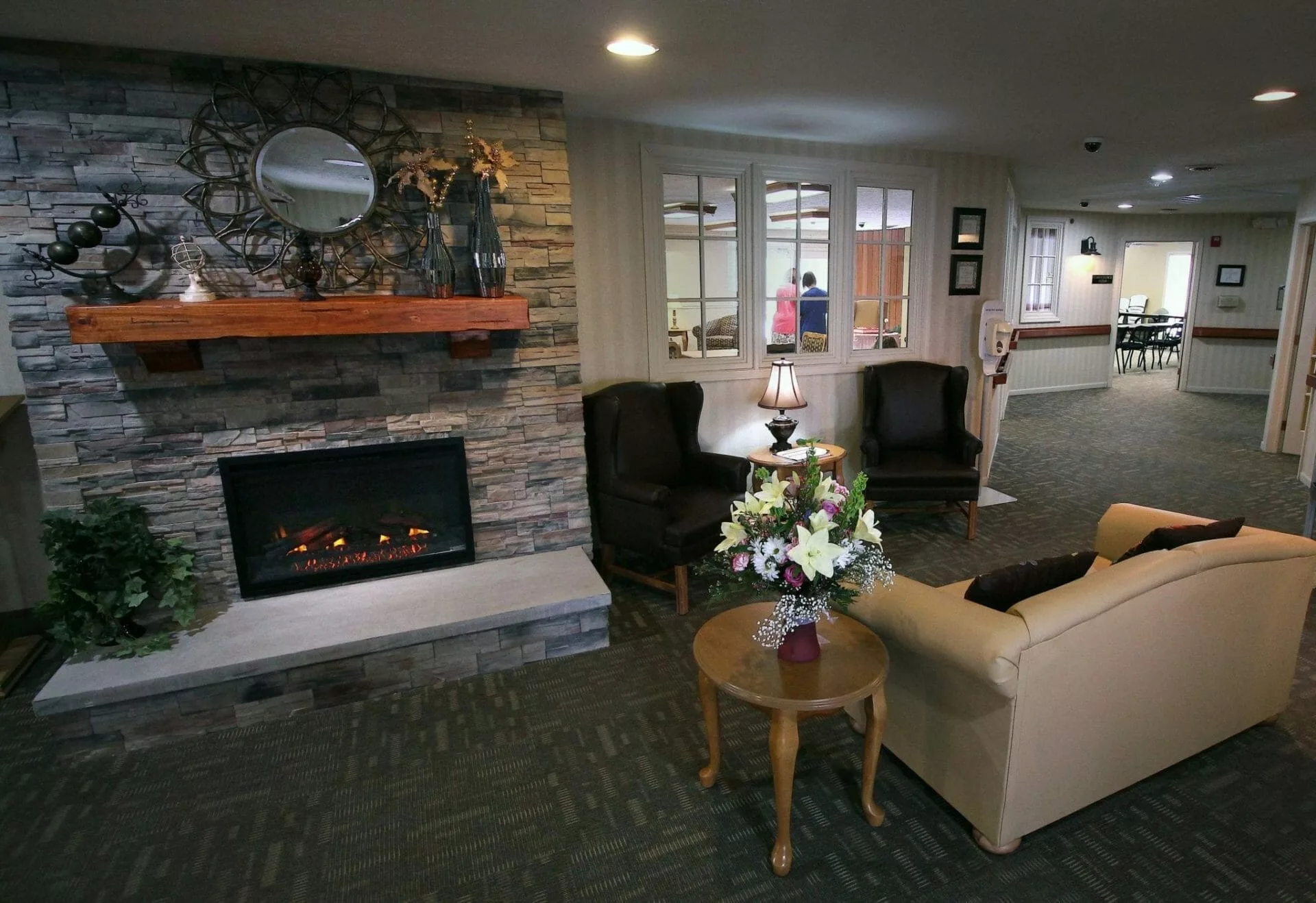 A cozy living room interior with a stone fireplace, armchairs, and a floral centerpiece on a wooden table.